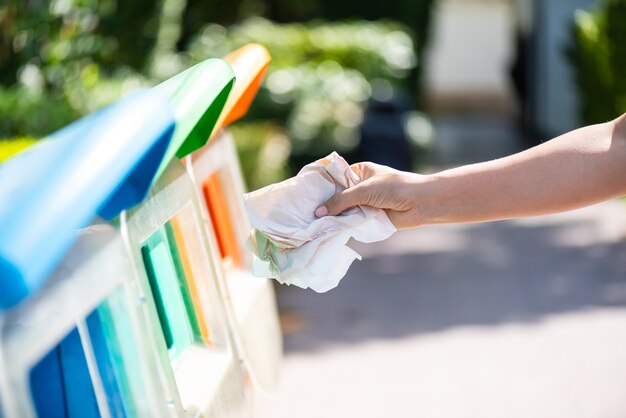 Foto mano della donna che tiene e che mette spreco della carta di emissione nei rifiuti dell'immondizia.