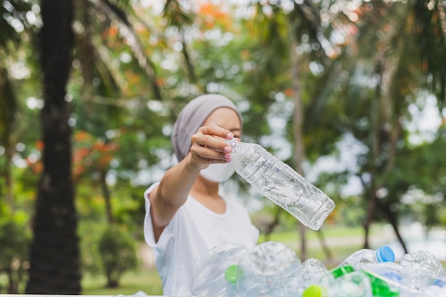 La mano della donna che tiene ricicla la bottiglia di plastica nell'ambiente del bidone della spazzatura concettuale