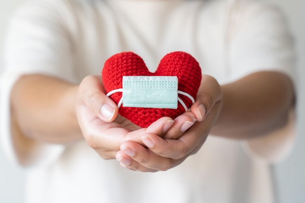 Foto mano della donna che tiene il cuore rosso che indossa una maschera protettiva