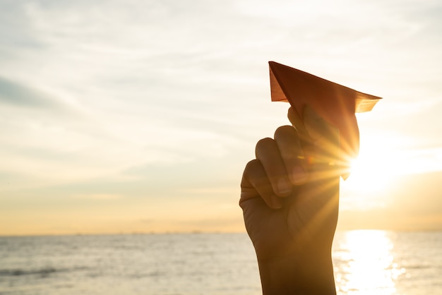 Woman Hand holding red paper rocket with blue sky background during sunset