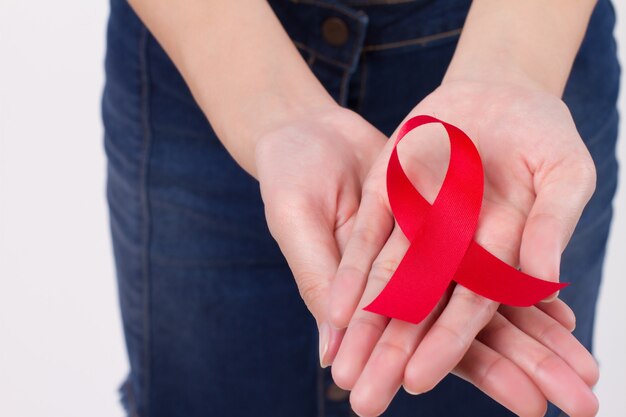 Woman hand holding red ribbon bow, hiv or aids awareness symbol presented by woman in studio shot. medical, charity, fund raising concept for red ribbon hiv aids day awareness