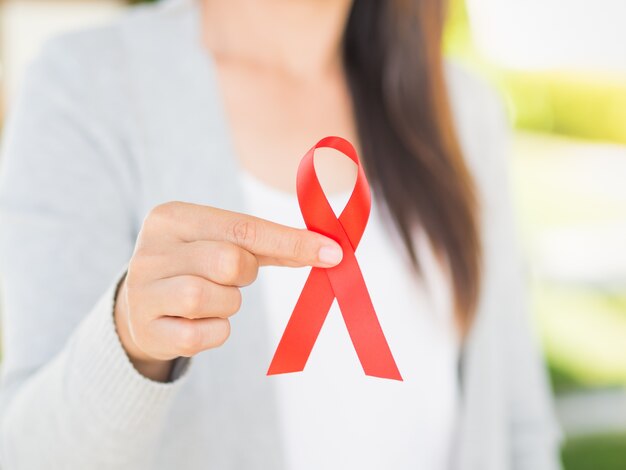 Mano della donna che tiene il nastro rosso hiv, nastro di consapevolezza di giorno di aids del mondo.