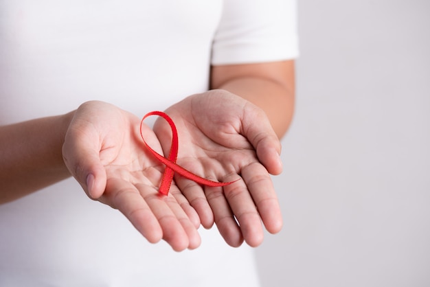 Mano della donna che tiene hiv rosso del nastro, consapevolezza di giornata mondiale contro l'aids