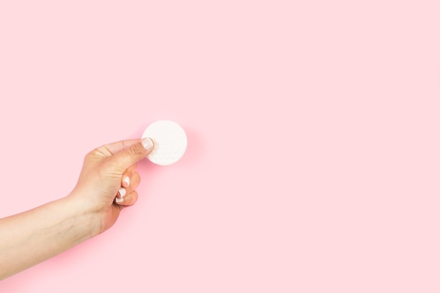 Woman hand holding a round cotton pad on a pink background with copy space