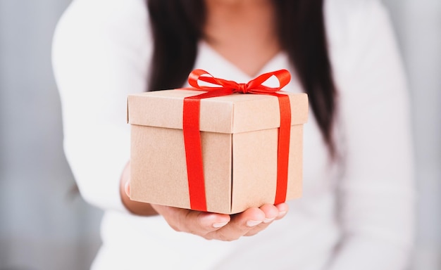 Woman hand holding rustic gift box presents tie with red ribbon bow Concept Season of giving