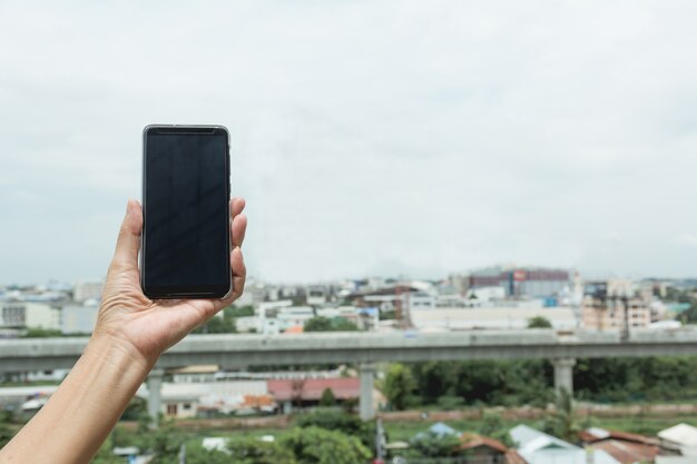 スマートフォンの建物の背景を持つ女性の手。