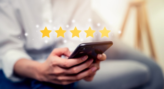 Mano della donna che tiene smartphone e valuta il tuo feedback e mostra cinque stelle sull'applicazione.