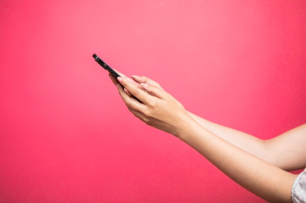 Woman hand Holding smartphone scroll and touch display on pink background.