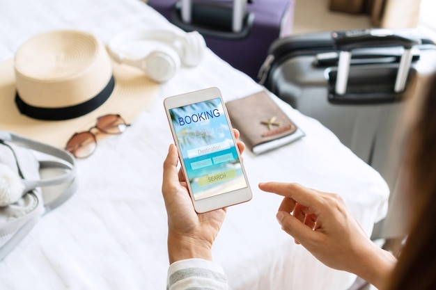 Woman hand holding smartphone with travel accessories on bed in hotel room Travel relaxation journey trip and vacation concepts Top view and copy space