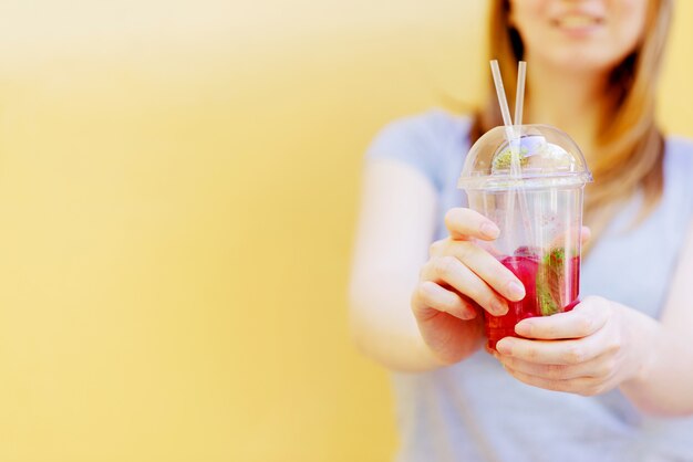 Woman hand holding smoothie shake against colored wall.