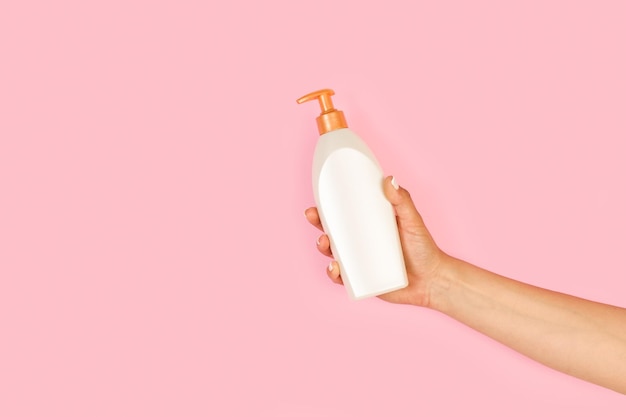 Woman hand holding a soap dispenser on a pink background with copy space