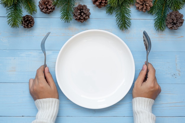 Woman hand holding spoon and fork over Empty plate with Christmas decoration