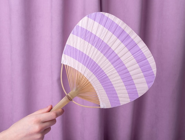 Woman hand holding utiva fan on violet background Japanese accessory for salvation from heat concept