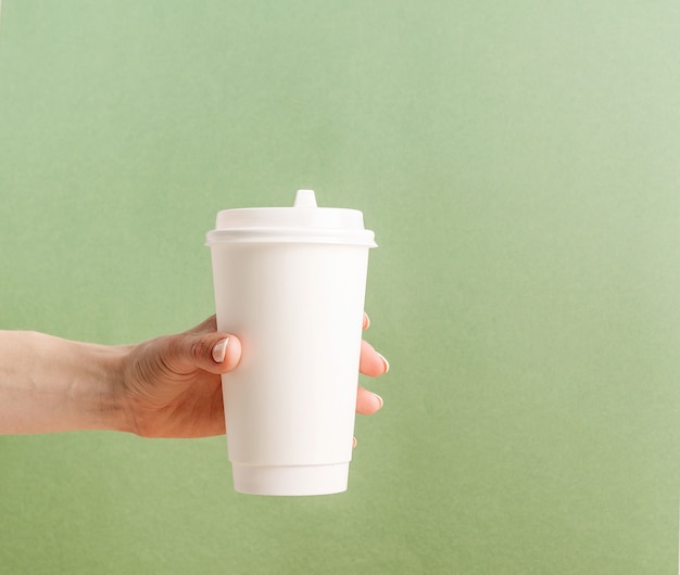 La mano della donna che tiene la tazza di caffè di carta da asporto grande bianca deride su su fondo verde