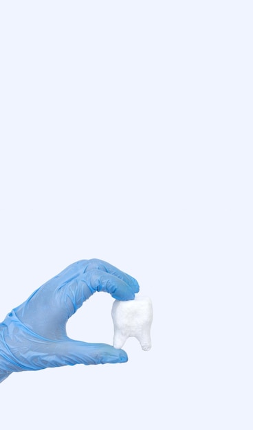 パステルブルーの背景に白い歯を持つ女性の手 歯科医の口腔病学の医療コンセプト