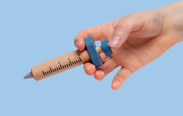 Woman hand holding wooden syringe model for medicine vaccine drugs injection on blue background Health care medical treatment concept