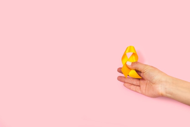 Woman hand holding a yellow ribbon on a pink background with copy space