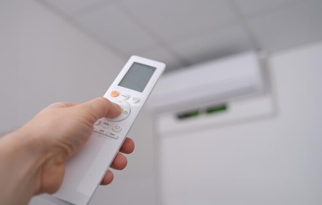 Woman hand holds remote control pointing at air conditioner in room Adjusted to ambient temperature