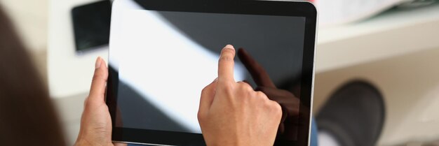 Photo woman hand holds tablet at home and controls finger across screen