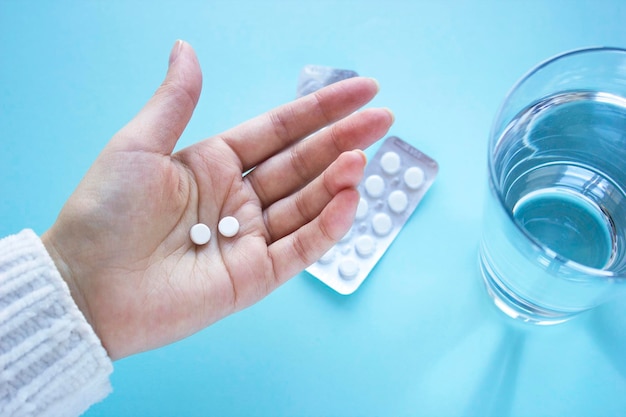 Woman hand holds two tablets with glass of water Woman drinks tablets Top view