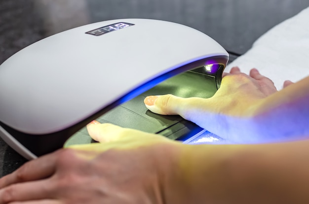 Woman hand inside nail lamp on table close-up. UV lamp for drying nails using the gel method. purple nails dried in a lamp.