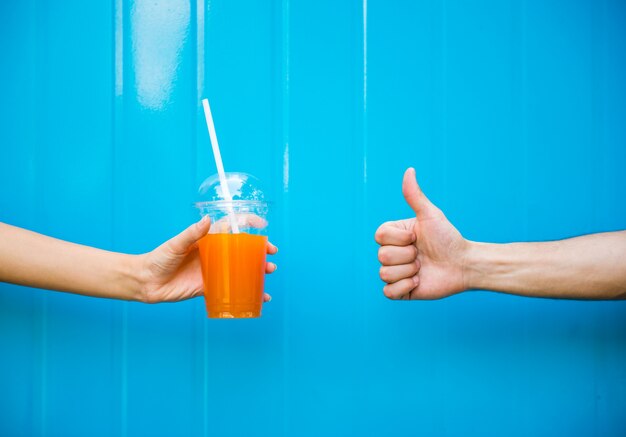 Woman hand is holding juice against the blue wall.