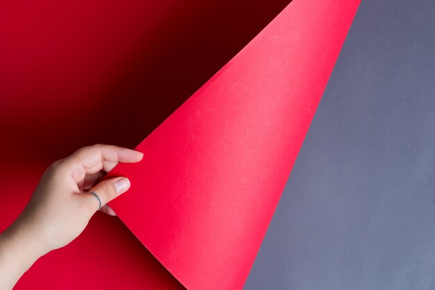 Рука женщины поворачивает красный бумажный лист на черной предпосылке с мягкими тенями.