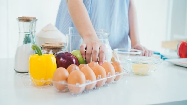 Photo a woman hand in the kitchen in a blue apron takes the egg out of the box