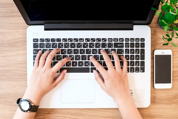 Mano della donna sulla tastiera del computer portatile con la vista superiore del monitor dello schermo in bianco.