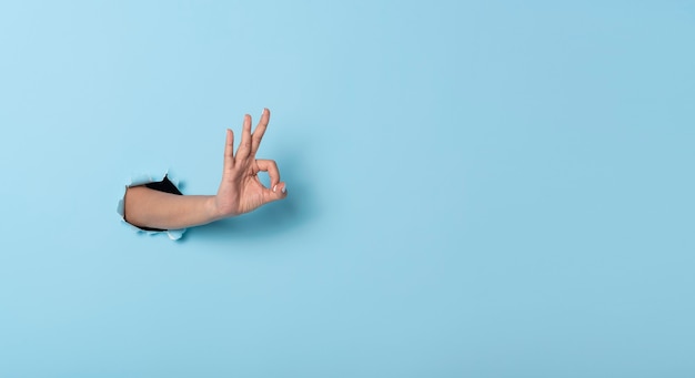 Woman hand makes a gesture OK in the wall on blue banner background.