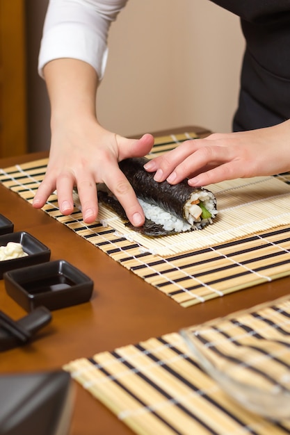 Woman hand moistening with water a sushi roll edge