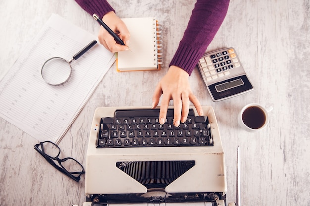 Woman hand notepad and typewriter on table