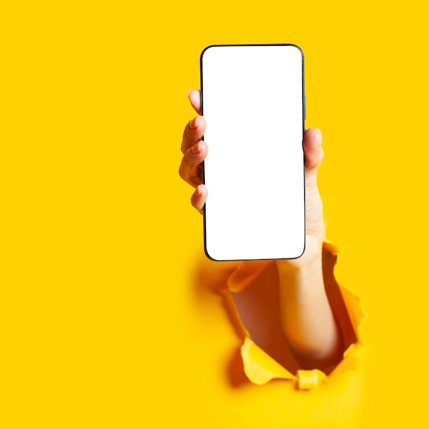 Woman hand in the paper hole holding smartphone Mobile application online shopping concept Isolated on yellow background