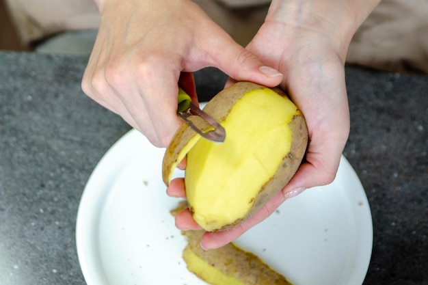 A woman hand peels potato with a knife closeup cooking fries top view