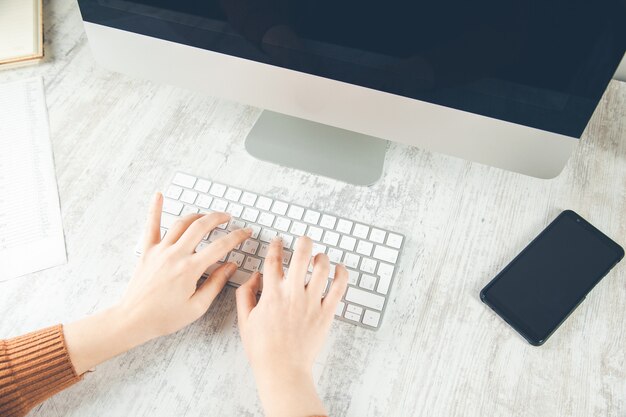 Telefono della mano della donna sulla scrivania del computer