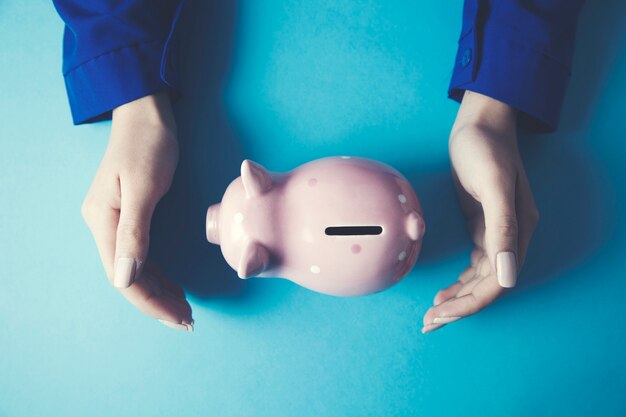 Woman hand piggy bank on blue table