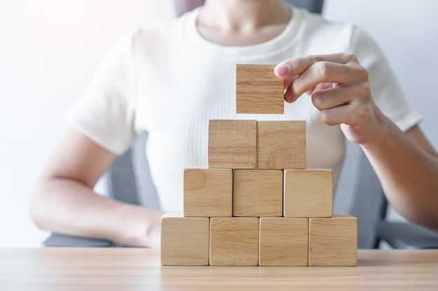 Woman hand placing wood block on the building Leadership Business process planning Risk Management and strategy Concepts