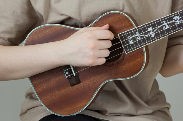 Woman hand playing body ukulele on the gray background