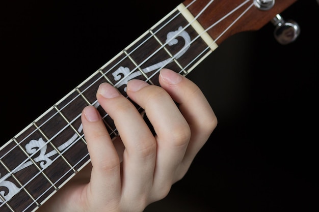 Woman hand playing ukulele on the black background