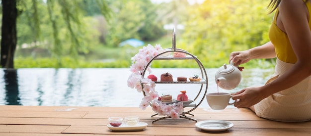 Woman hand pouring hot tea with Afternoon tea set and Pink dessert at luxury hotel