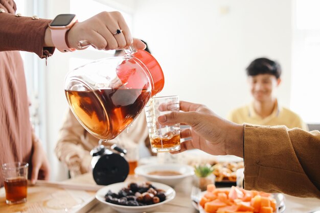 Woman hand pouring tea from tea pot into a glass when having iftar dinner