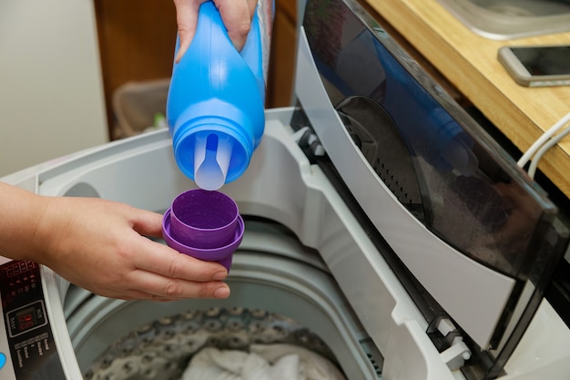 Woman hand pours liquid powder into the drum of the washing machine laundry