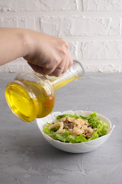 Woman hand pours olive oil on fresh warm seafood salad and lettuce