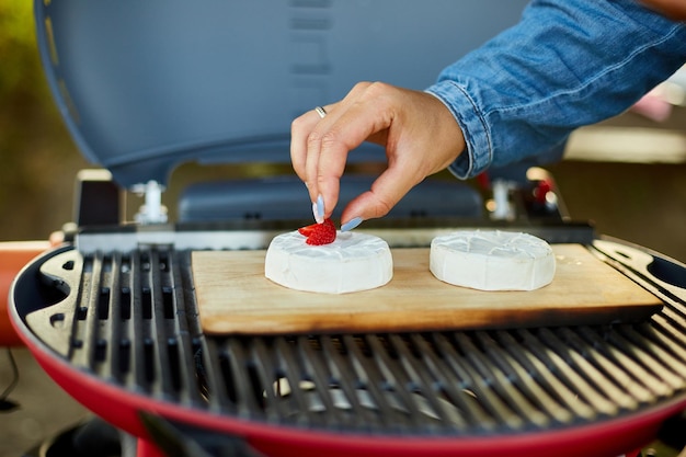 Woman hand put strawberry on grill camembert cheese outdoor