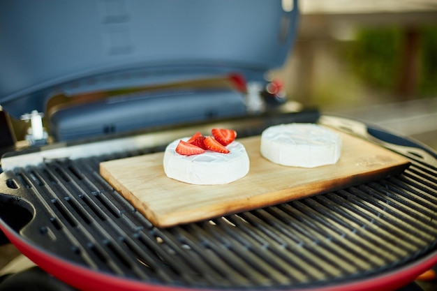 Woman hand put strawberry on grill camembert cheese outdoor