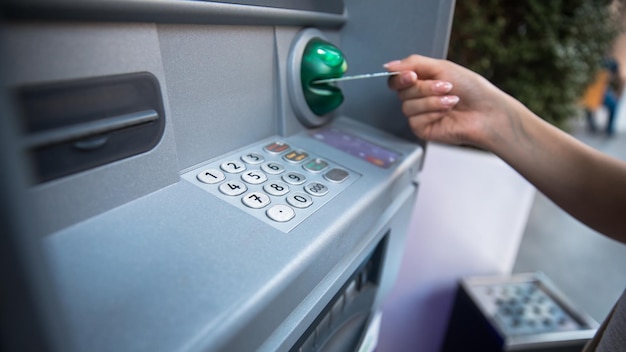 Woman hand puts credit card into ATMxA