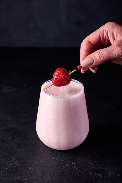 Woman hand puts strawberry on lassi is traditional indian cold refreshing drink with yoghurt berry