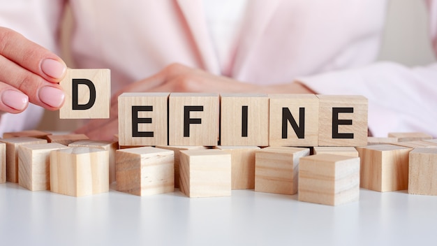 The woman hand puts a wooden cube with the letter D from the word Define