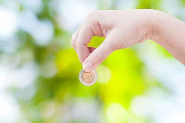 Woman hand putting a coin on green nature