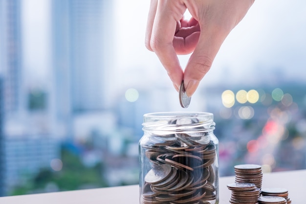 Woman hand putting coin into glass of bottle for saving money